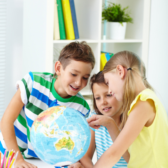 Studying geography Portrait of curious classmates at workplace studying globe in classroom
